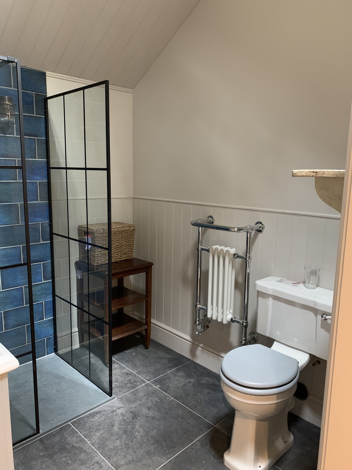 Walk-in shower lined in blue subway tile, with a black Crittall-style screen