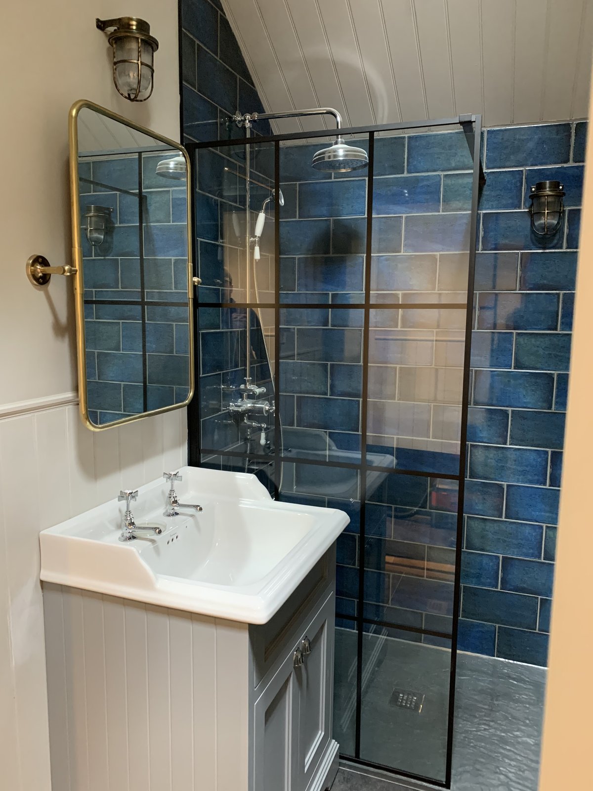Walk-in shower lined in blue subway tile, with a black Crittall-style screen