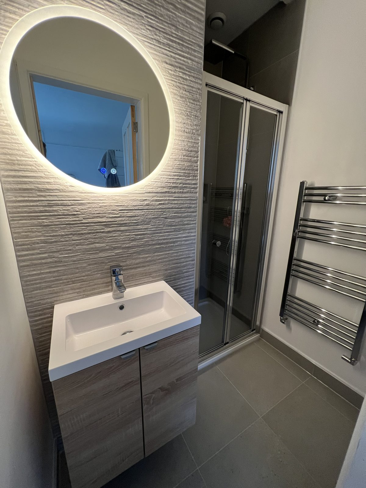 Bathroom with an oak-effect vanity, round lit mirror and a glass shower screen