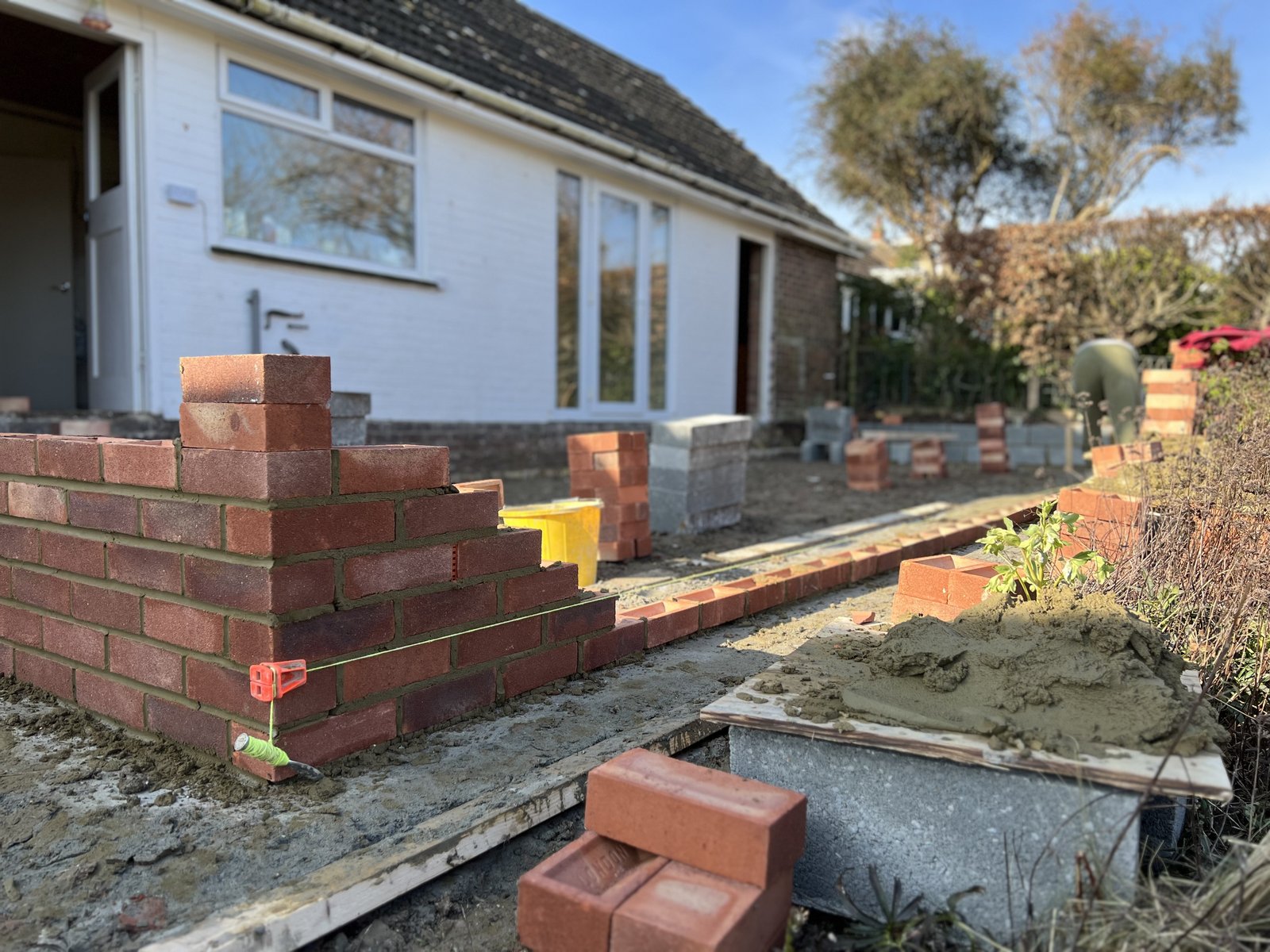 Red brickwork started on a string line in a garden, beside a white house