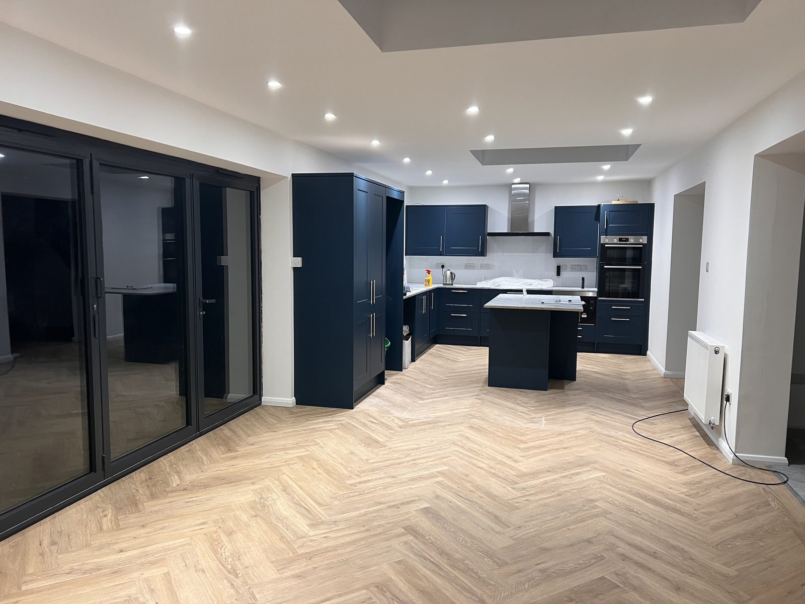 Navy kitchen with a central island, herringbone wood floor and dark-framed patio doors