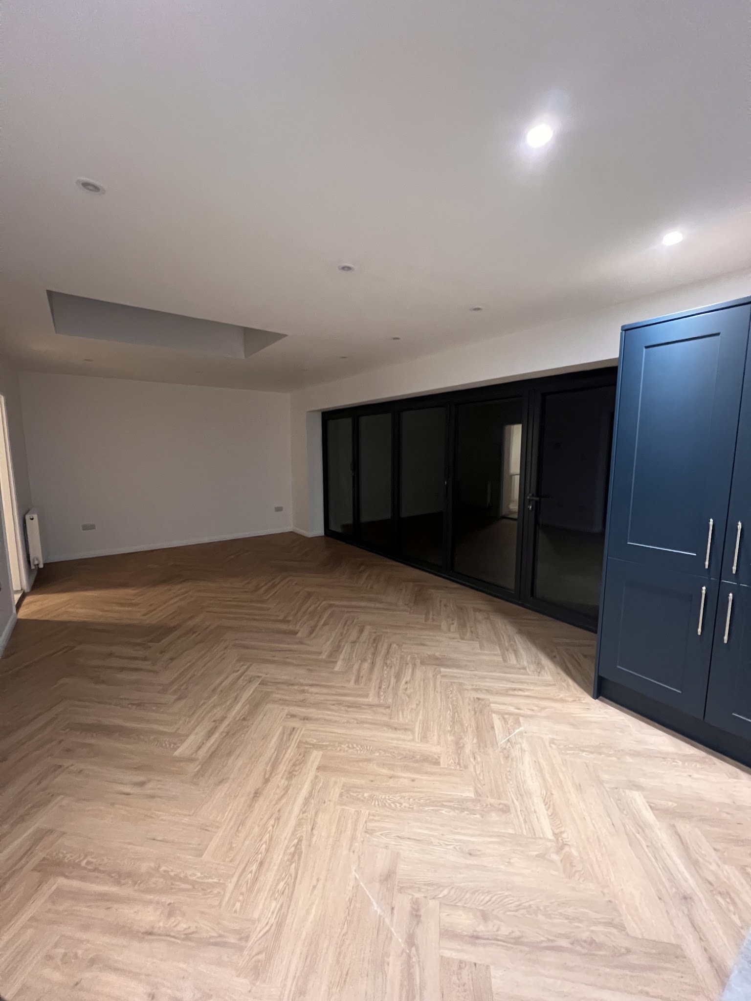 Open living space with herringbone flooring, bifold doors and cabinetry